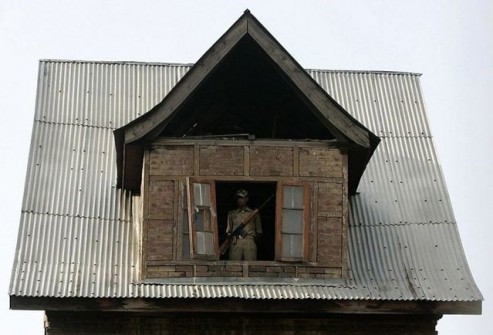 An Indian policeman stands guard at the top of a house during a ceremony to mark Martyrs Day in Srinagar